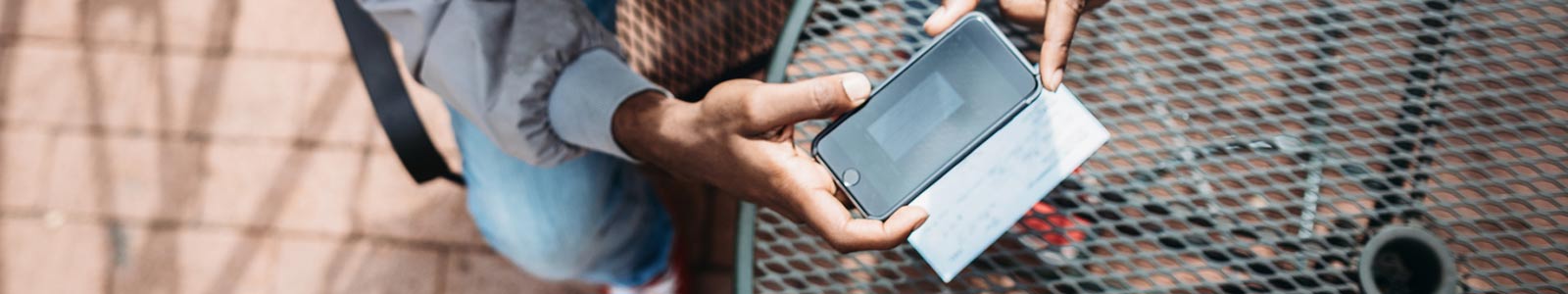 Man sitting outside, taking photo of a check with his cellphone.