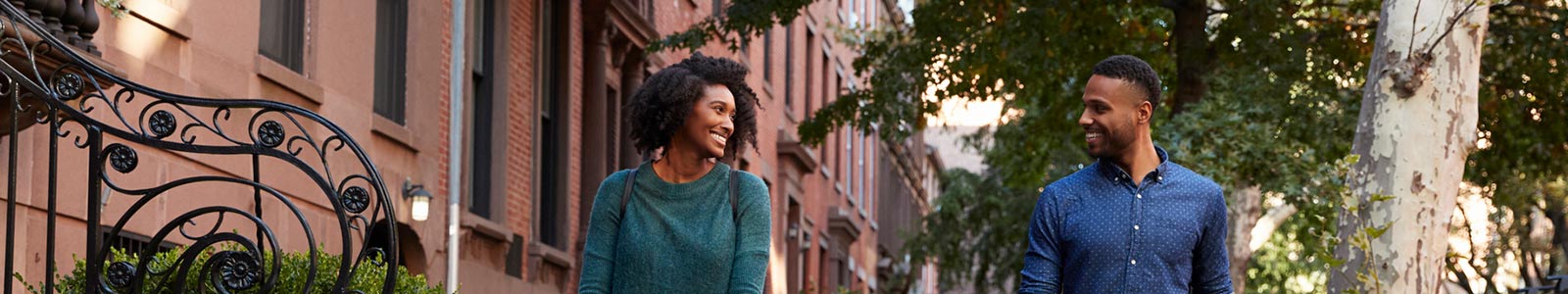 Couple walking on sidewalk outside, smiling and looking at eachother.