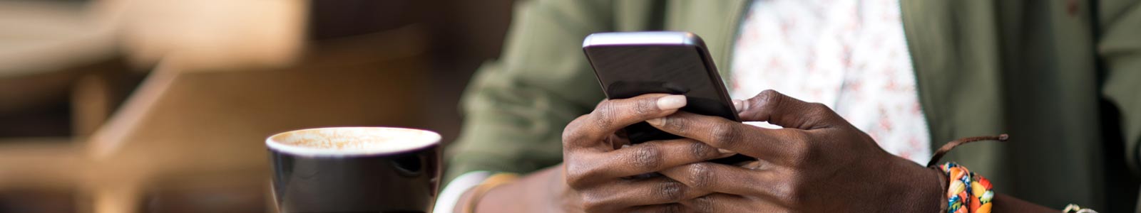 Woman with coffee cup, using mobile phone, inside.