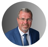 A picture of a man wearing glasses and a suit smiling. 