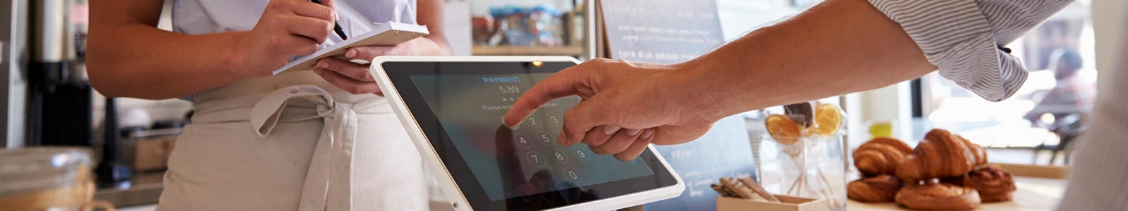 business owner taking an order while customer types on tablet inside.